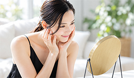 鏡の前で頬に手を添え、日々のスキンケアをする女性